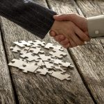 Closeup of male and female business partners shaking hands over a pile of puzzle pieces